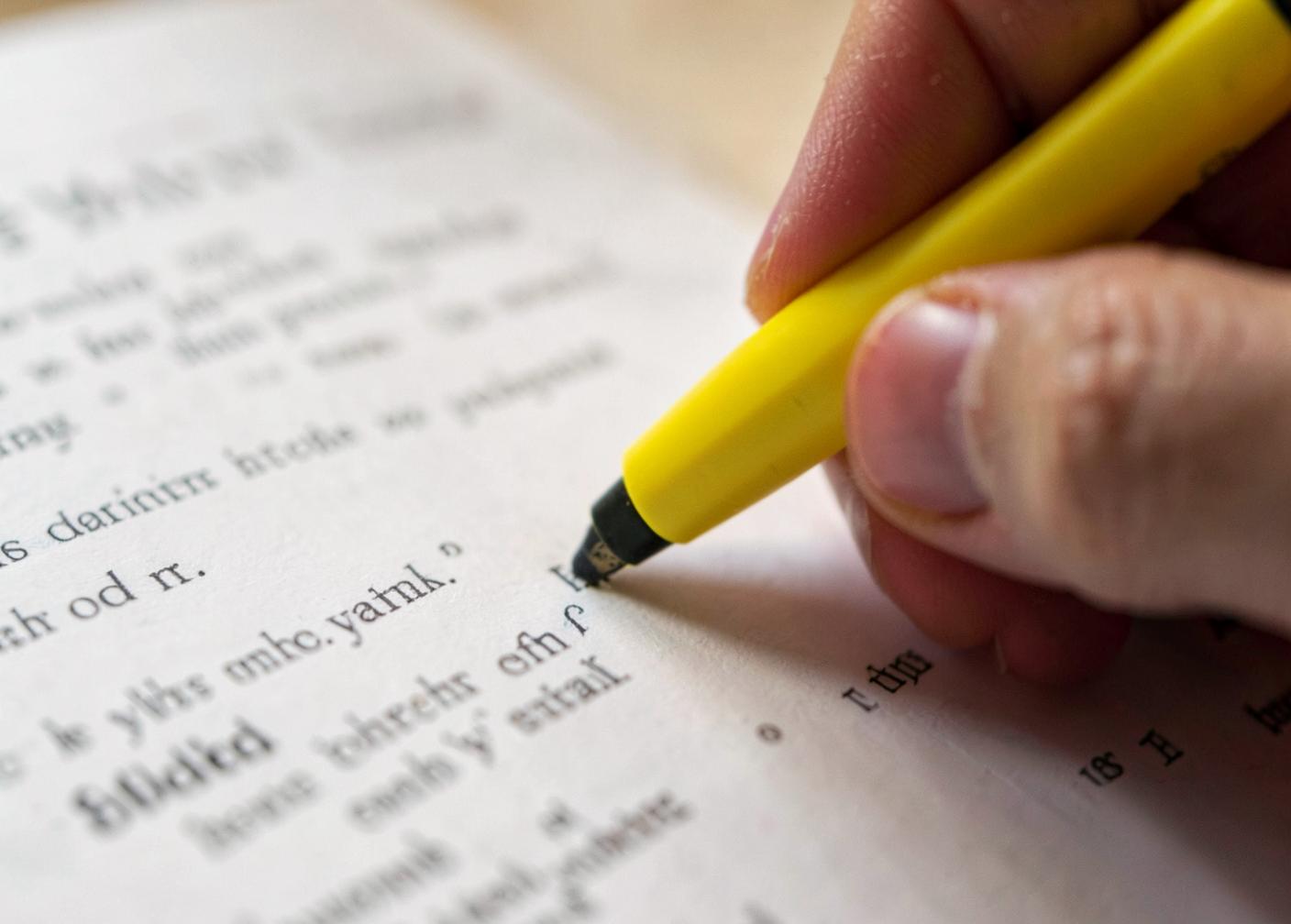 Hand using a yellow highlighter to mark one short passage on a printed page